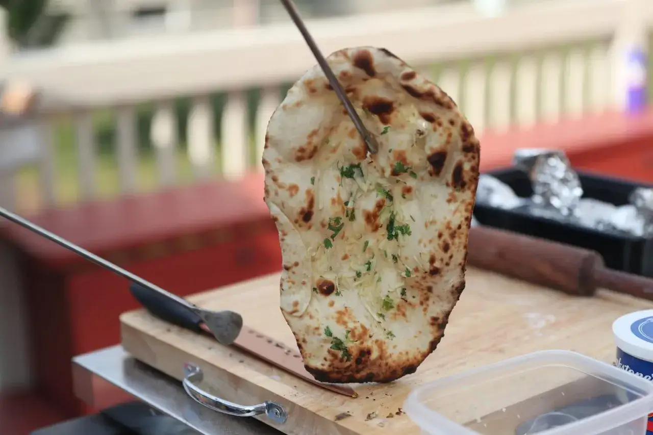 Chrupiący chlebek naan, świeżo wyjęty z pieca tandoori, posypany ziołami i serem.