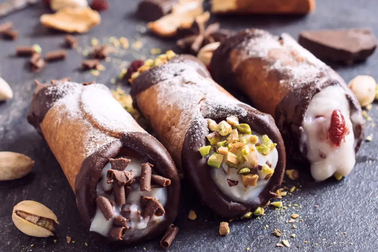 Trzy pyszne cannoli z kremem, posypane cukrem pudrem, pistacjami i czekoladą. Idealne na deser, gdy szukasz sprawdzonego cannoli przepis.