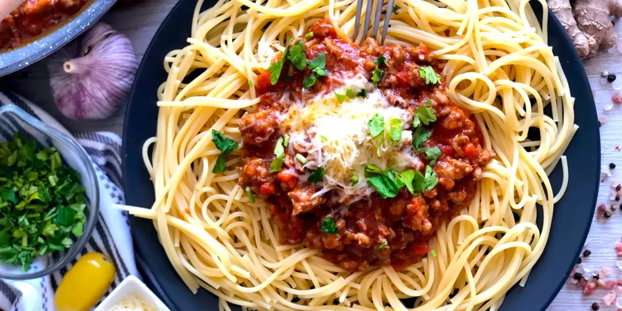 Pyszne spaghetti bolognese, prosty przepis na obiad. Danie posypane serem i natką pietruszki.