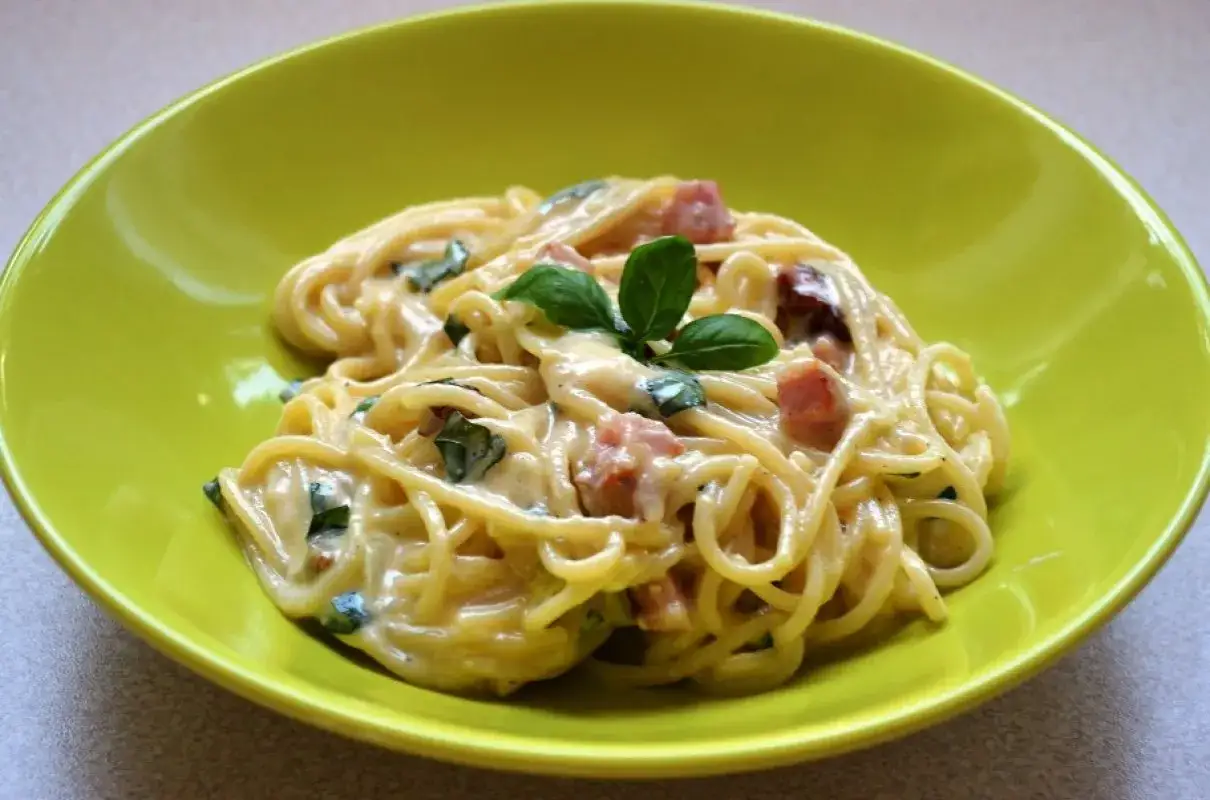 Spaghetti carbonara ze śmietaną, podane w zielonej misce, ozdobione bazylią. Pyszny przepis na klasyczne danie.