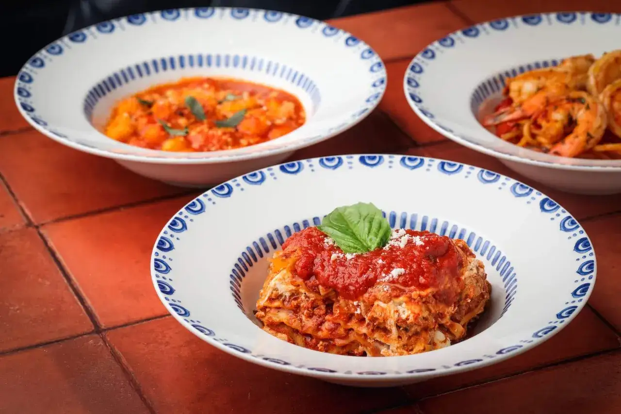 Lasagne, krewetki z makaronem i gnocchi w sosie pomidorowym – apetyczne włoskie dania w ozdobnych miskach.