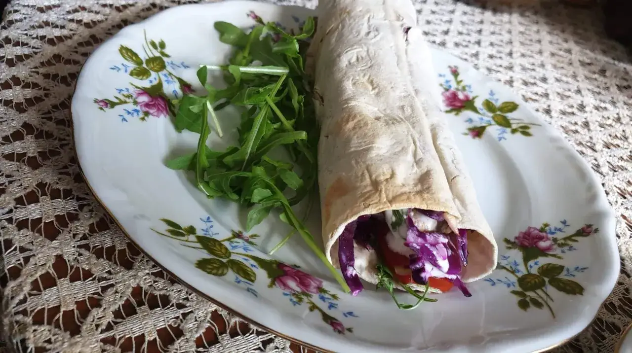 Pyszny lawasz kebab z czerwoną kapustą i rukolą na talerzu z kwiatowym wzorem.