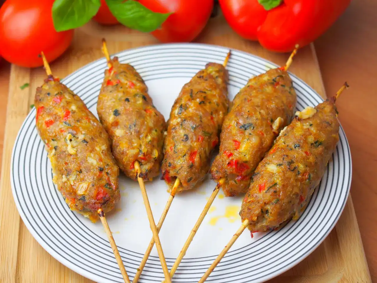 Pięć soczystych kofta kebabów na patyczkach, z widocznymi kawałkami papryki i ziół, podanych na talerzu z czarno-białymi paskami.