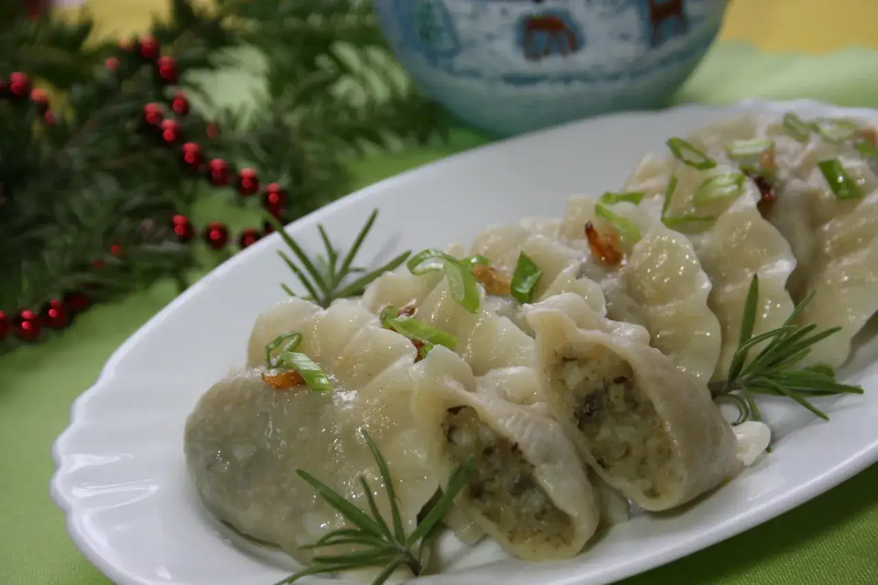 Pyszne pierogi ukraińskie, udekorowane szczypiorkiem i rozmarynem, prezentują się apetycznie na białym talerzu.