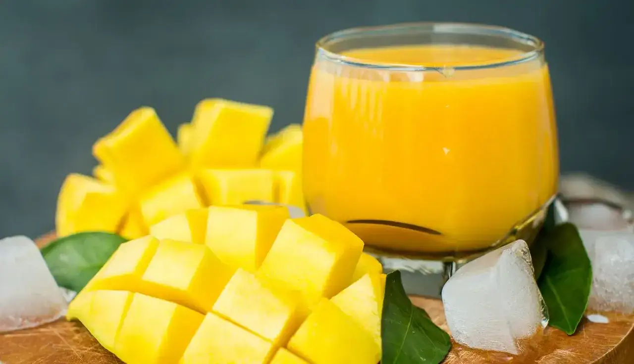 Orzeźwiający mango lassi w szklance, obok pokrojonego w kostkę mango, liści i kostek lodu. Idealny na upalne dni.