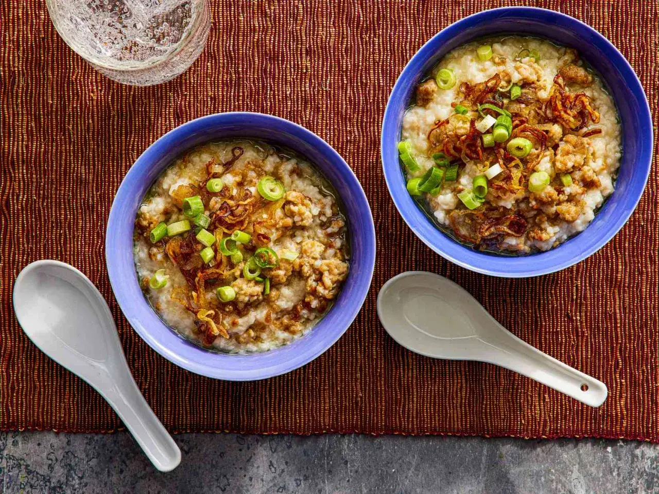 Dwie miseczki aromatycznego congee z mielonym mięsem, chrupiącą cebulką i szczypiorkiem.