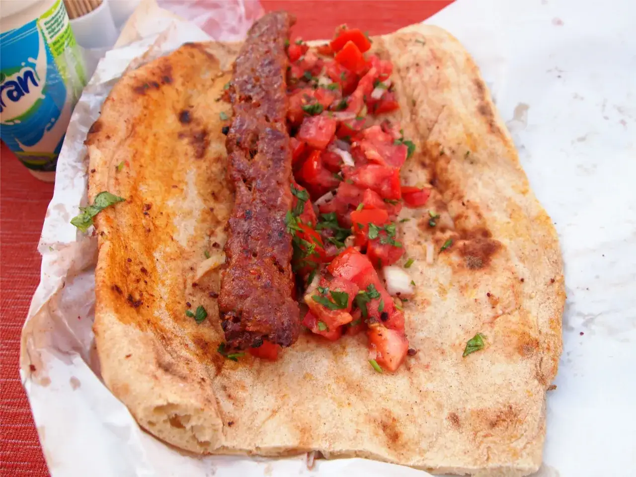 Pyszny turecki kebab z soczystym mięsem, świeżymi pomidorami i natką pietruszki, podany na ciepłym placku.