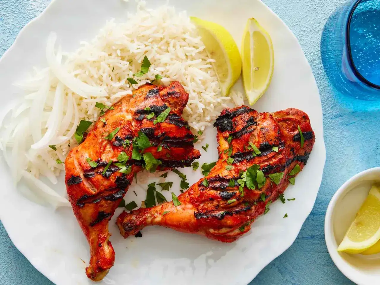 Dwa soczyste kawałki kurczaka tandoori z ryżem, cebulą i cytryną na talerzu.