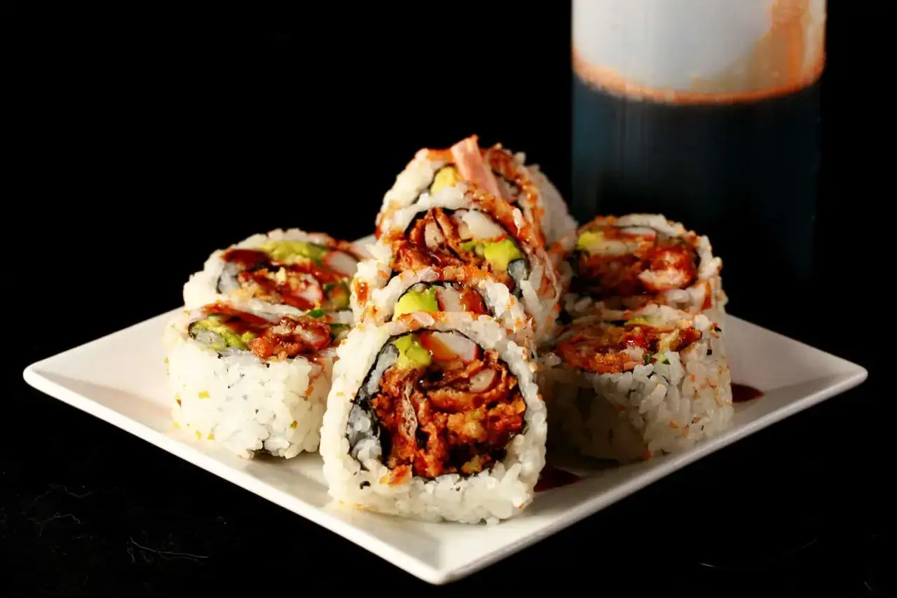 Roladki sushi z awokado i krewetkami, polane sosem do sushi, na białym talerzu.