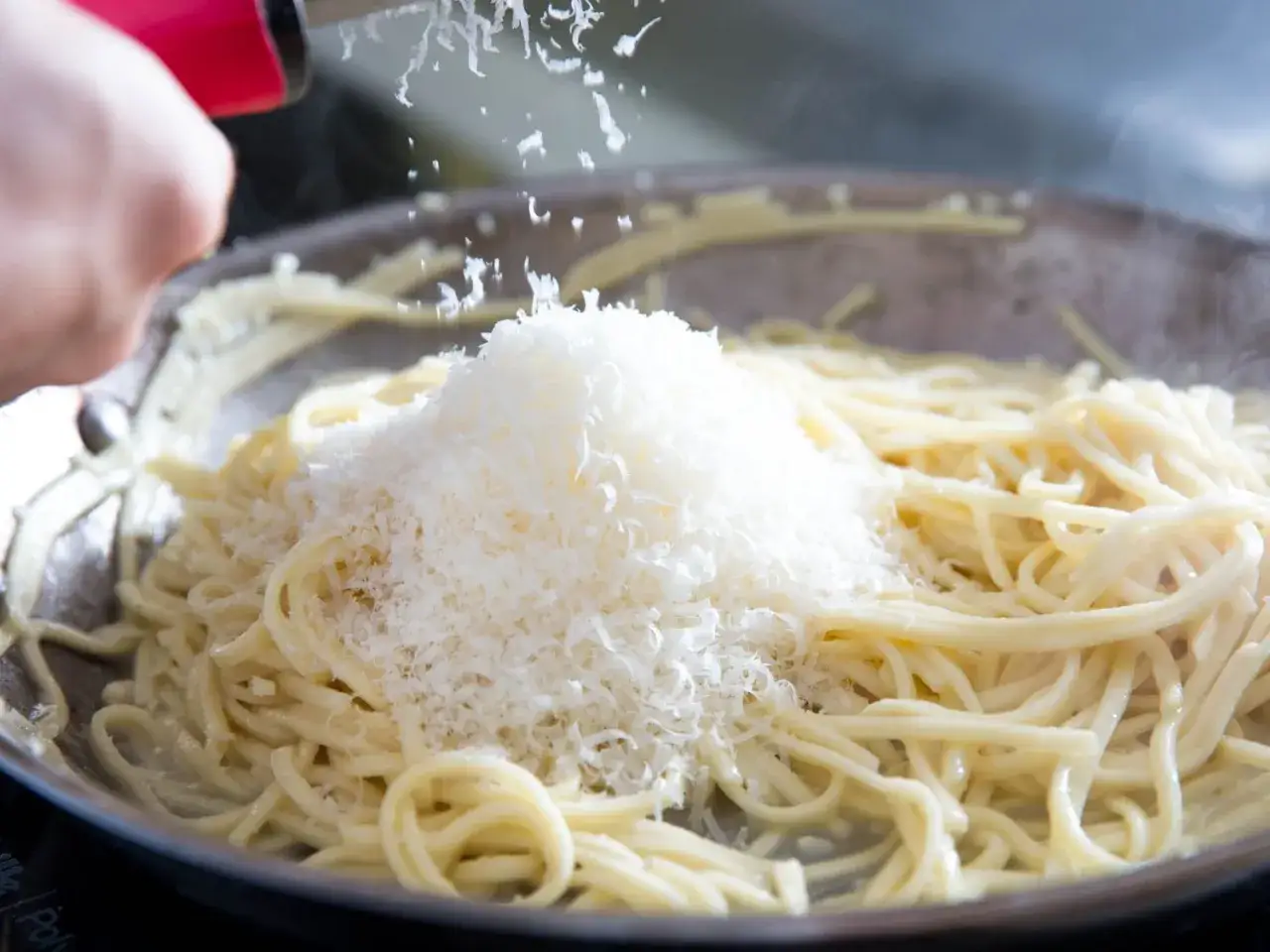 Szukając alternatywy, jaki ser do spaghetti zamiast parmezanu? Na zdjęciu widać, jak starty ser trafia na gorący makaron.