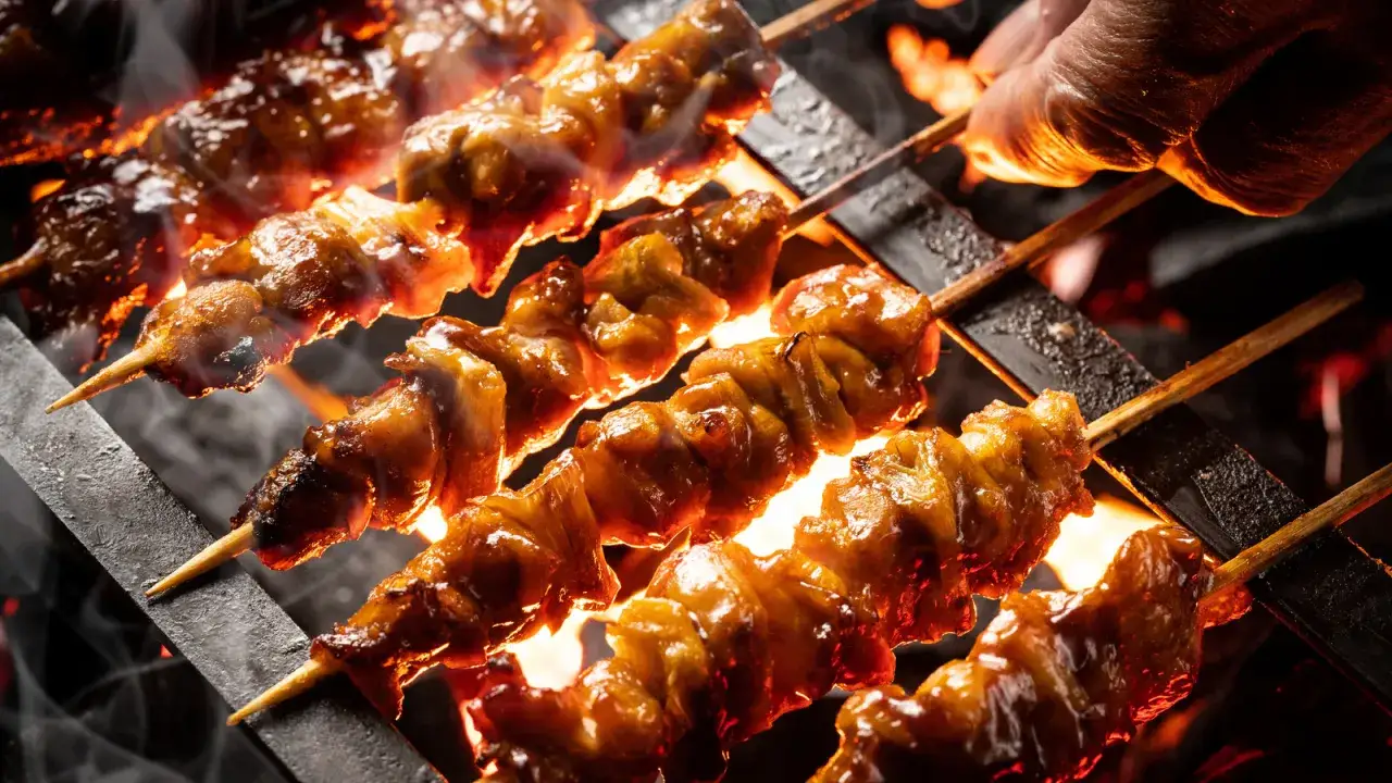 Soczyste yakitori skwierczy nad żarem, dym unosi się, a ręka obraca szaszłyki, by równomiernie się upiekły.