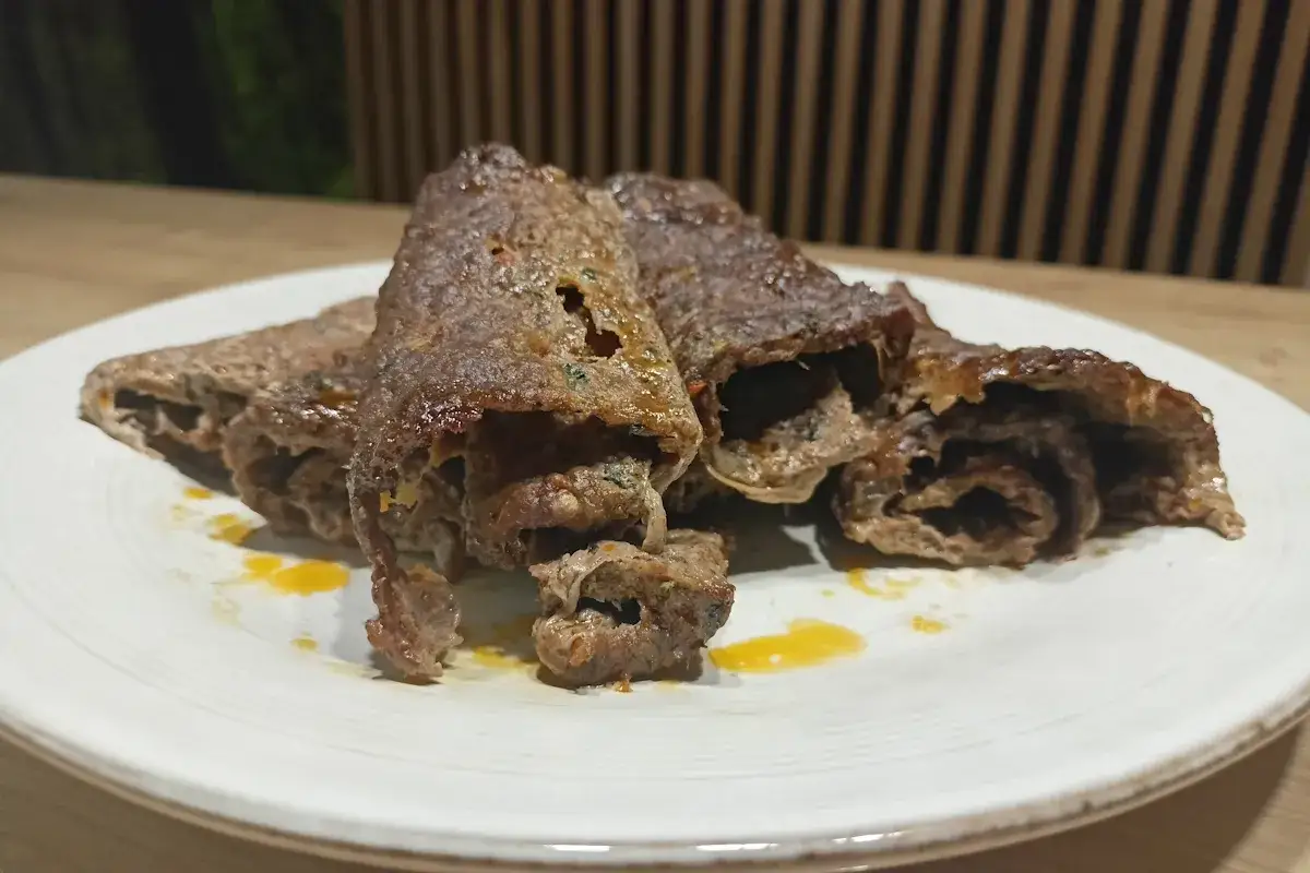 Pyszny, domowy kebab z piekarnika, soczyste mięso zawinięte w cienkie plastry, podane na talerzu z żółtym sosem.