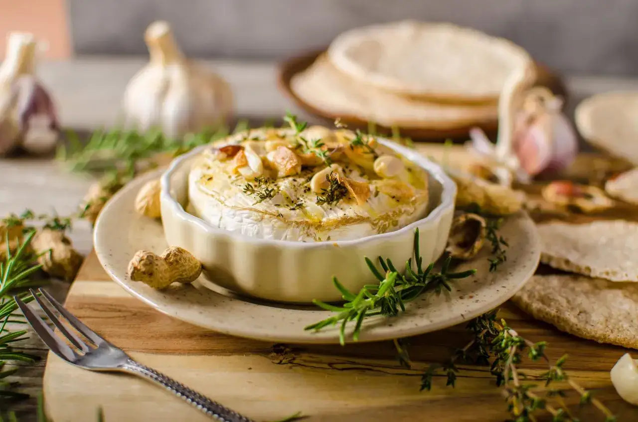 Pyszny camembert z grilla, zapieczony z czosnkiem i ziołami, podany z orzeszkami i chrupkim pieczywem. Idealny na przekąskę.