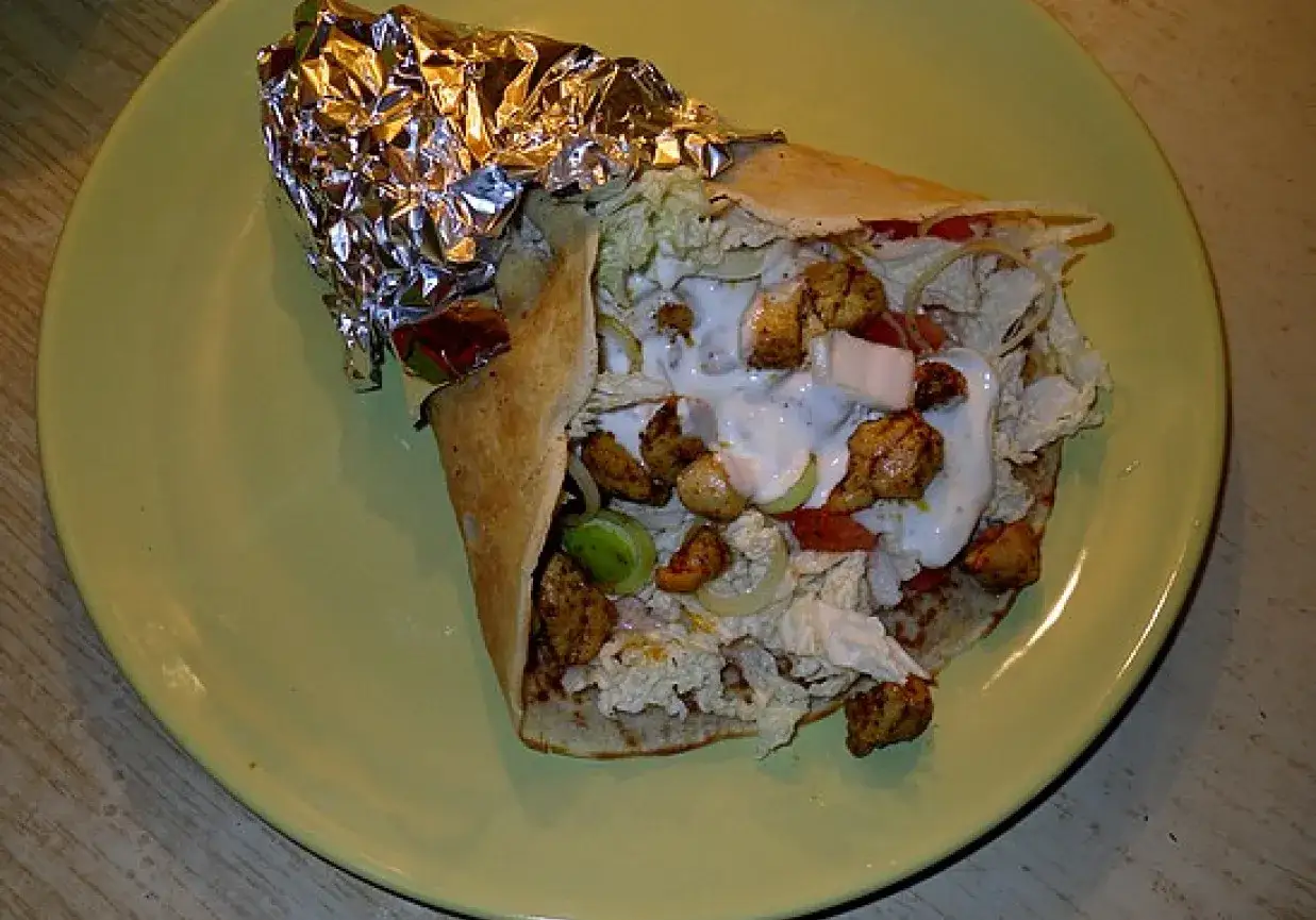 Pyszny kebab w tortilli z kurczakiem, warzywami i sosem na żółtym talerzu.