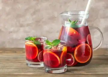 Dzbanek i dwa kieliszki z sangrią, owocami i miętą na drewnianym stole.