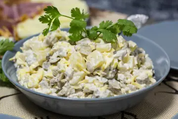 Sałatka z pieczarkami, jajkiem i serem w szarej misce, ozdobiona natką pietruszki.
