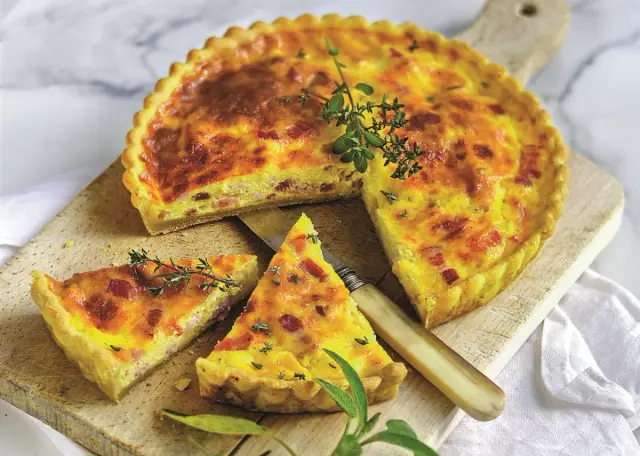 Francuski kisz z boczkiem i ziołami na desce, z odciętym kawałkiem.