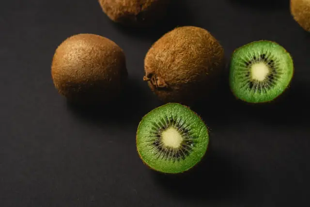 Kilka owoców kiwi, w tym dwa przekrojone na pół, na ciemnym tle.